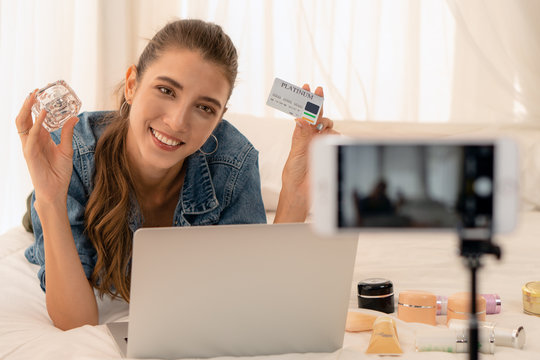 youtuber woman presenting cosmetic products to followers as youtuber by boardcasting using smartphone and holding cardit card showing payment method