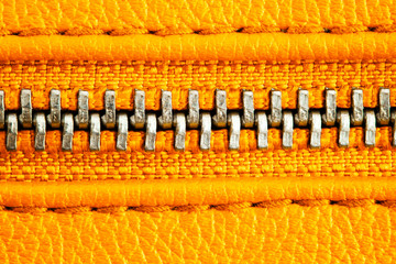 Metal zipper on intense orange leather jacket or purse detail close up macro. The zipper is tightly...