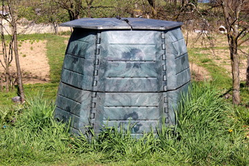 Plastic compost bin with dilapidated faded color surrounded with uncut grass and trees in local...