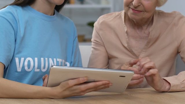 Female volunteer and retiree scrolling tablet, online application for pensioners
