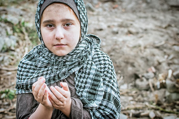 Fototapeta premium a refugee child in the war, a Muslim girl with a dirty face on the ruins, the concept of peace and war, the child is crying and waiting for help.