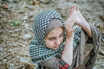 a refugee child in the war, a Muslim girl with a dirty face on the ruins, the concept of peace and war, the child is crying and waiting for help.