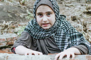 a refugee child in the war, a Muslim girl with a dirty face on the ruins, the concept of peace and war, the child is crying and waiting for help.