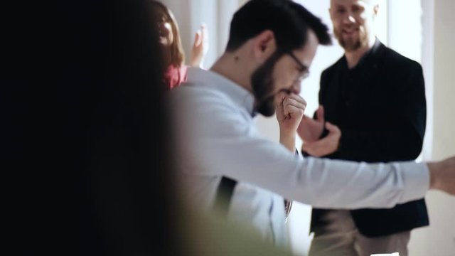 Happy young Caucasian male boss walks along modern light office giving high fives to partners after career achievement.