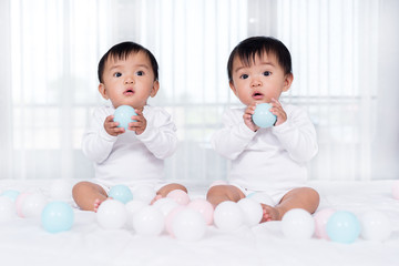 cheerful twin babies playing color ball on  bed