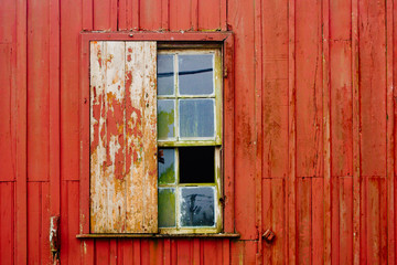 Broken glass and wood window from abandoned house facade with old peeling red wooden wall and grungy surface texture.