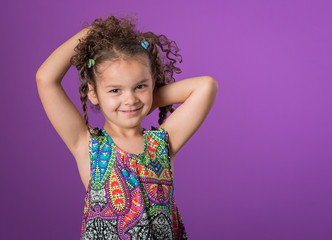 Mixed race little girl arms raised to her curly brown hair isolated on purple background - 281352886