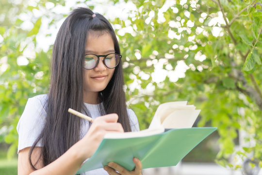 asian female hand writing something on the paper and nature background.teenage smile and relaxed use pencil and notebook in a park nature background