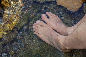 Feet immersed in the clear water with small rocks of a mountain river.