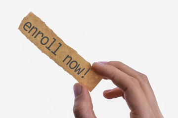 Blank torn notepaper in hand with text  writing Enroll Now