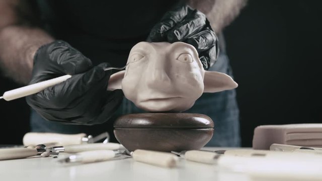 Artist models a plasticine puppet head with a clean up tool.