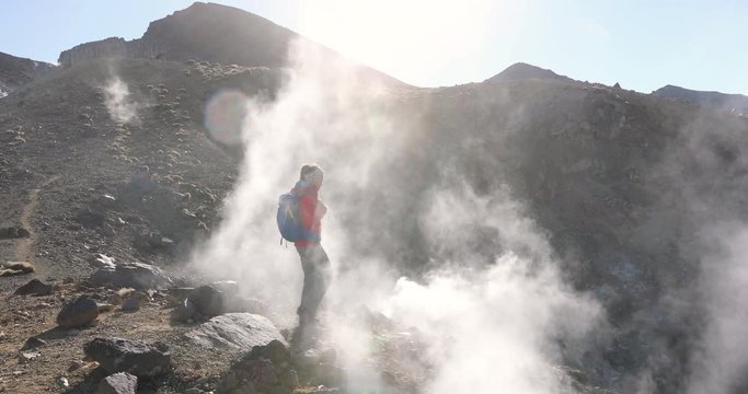 People walking on active volcano with smoke and fumes, tramping track at Tongariro National Park in New Zealand. Woman backpacker on hike hiking in mountains. 59.94 FPS slow motion.