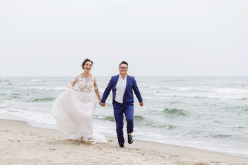 Fototapeta na wymiar newlyweds run along the beach along the sea in cloudy weather