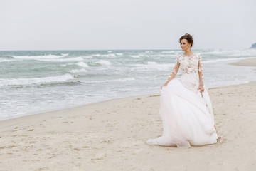 Fototapeta na wymiar Young beautiful bride with a long dress walks on the sea beach