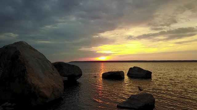 Flying towards a bright sunrise over big rocks and a colorful sea.