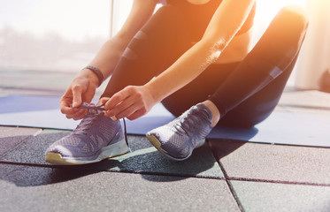 Woman tying the laces of sport sneakers sitting on a mat in the gym