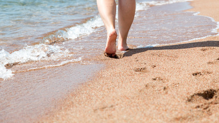 Closeup of bare feet on the beach. Walking on the sand at the water's edge. Vacation and travel concept.