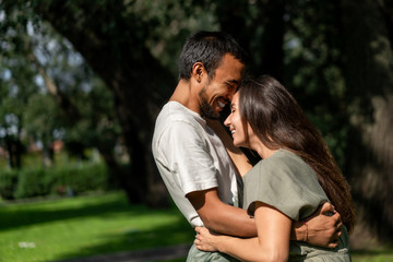 Obraz premium Mixed couple in love is hugging in park during warm summer sunny weather. friend and girlfriend different races love each other. Tolerance, world peace. Lifestyle