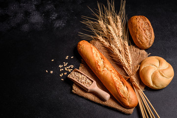 Fresh fragrant bread with grains and cones of wheat against a dark background. Assortment of baked...
