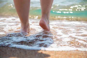 Closeup of bare feet on the beach. Walking on the sand at the water's edge. Vacation and travel...