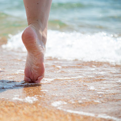 Closeup of bare feet on the beach. Walking on the sand at the water's edge. Vacation and travel concept.