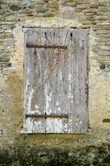 Old house window with closed unpainted shutter in textured rock wall