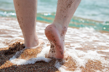 Closeup of bare feet on the beach. Walking on the sand at the water's edge. Vacation and travel...