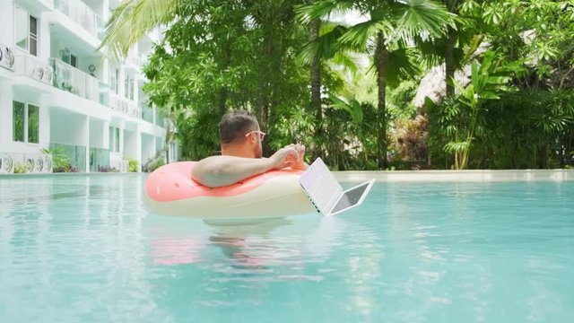 Fat funny man in pink inflatable circle surprised and drops the laptop into the water in the pool.