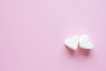 Two white hearts on a pink background. White heart-shaped marshmallows.