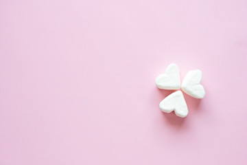 White heart-shaped marshmallows. Three white hearts on a pink background.