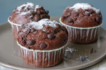 Three chocolate muffins lie on a plate against the background of a turquoise-colored table. Celebration. Birthday. Christmas and New Year.