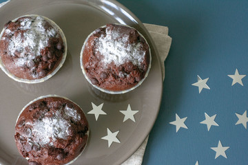 Three chocolate muffins lie on a plate against the background of a turquoise-colored table. Celebration. Birthday. Christmas and New Year.