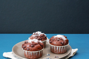 Three chocolate muffins lie on a plate against the background of a turquoise-colored table. Celebration. Birthday. Christmas and New Year.