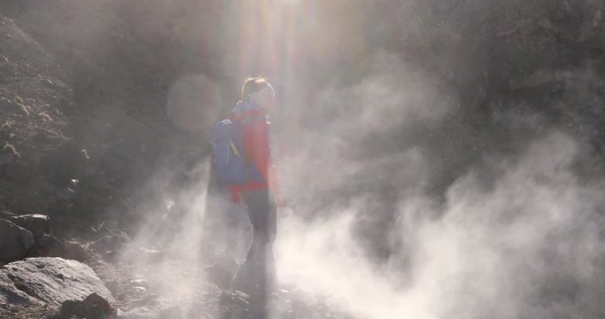 Woman hiking on active volcano with smoke and fumes, tramping track at Tongariro National Park in New Zealand. Woman backpacker on hike walking in mountains. 59.94 FPS slow motion.
