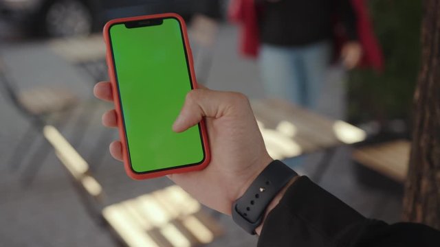 Busy young man holding using a modern smartphone with green chromekey screen for copy space outdoors in the city. People life and technology.