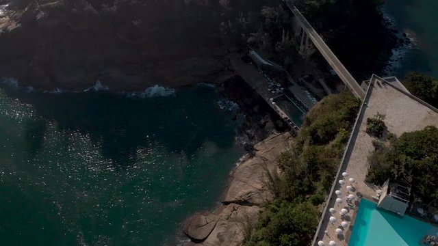 Top down aerial view of a recreational rooftop swimming pool on a small island on the coast of Rio de Janeiro seen from above at sunset with umbrellas casting a shade