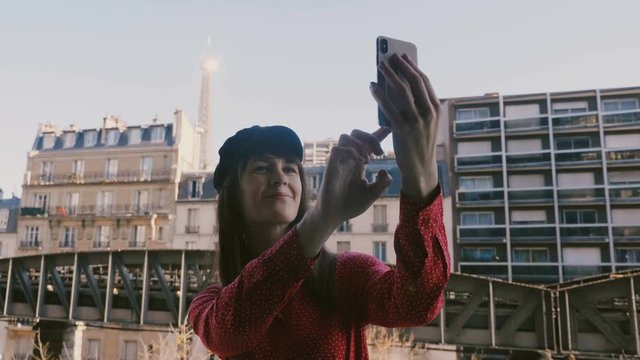 Happy beautiful smiling tourist woman taking smartphone selfie photo with Eiffel Tower view in Paris from room balcony.