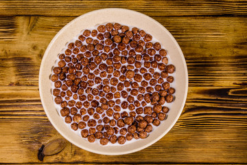 Ceramic plate with chocolate cereal balls in milk on wooden table. Top view