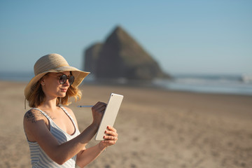 A young girl in sunglasses draws standing on a tablet on the ocean at sunset, freelancing, making money on the Internet, getting money on the Internet