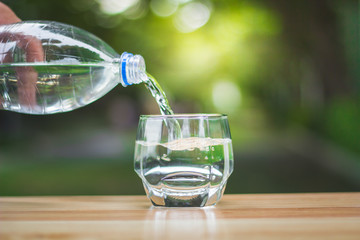 Pouring  purified drink water from the bottle on table over sunlight and natural green background
