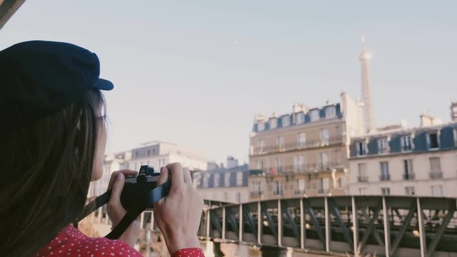 Happy professional photographer woman in red dress taking a photo of the Eiffel Tower view in Paris with vintage camera.