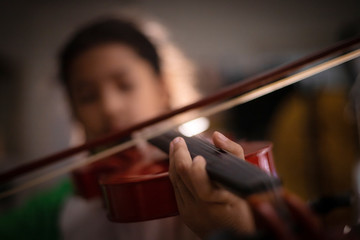 Close-up shot little girl playing violin orchestra instrumental with vintage tone and lighting effect dark and grain processed select focus shallow depth of field © Kaikoro