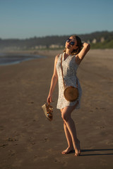 A young girl in sunglasses walks along the beach of the ocean at sunset, lifestyle, walk, rest, sunny light