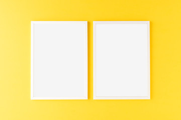 Two empty photo frames hanging on yellow wall. Mockup