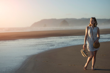 Young girl in sunglasses walks on the beach of the ocean at sunset, lifestyle