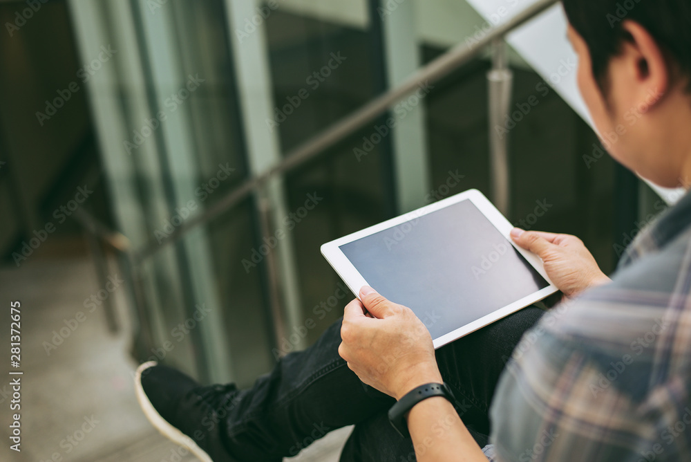 Poster man in black jeans sitting on staircase and holding tablet computer with touch screen,man using bank