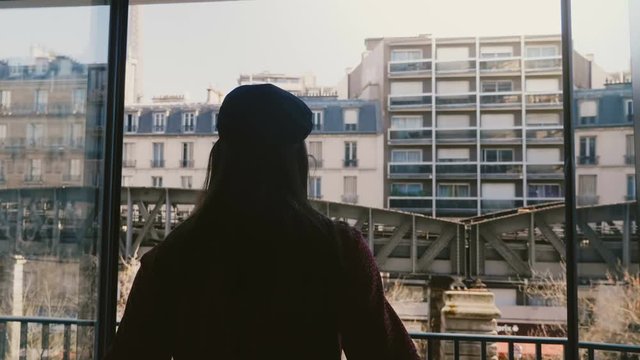 Camera follows young happy woman silhouette walking to open balcony window, enjoy sunny Eiffel Tower view slow motion.