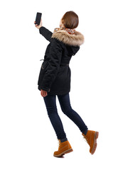 Back view woman in winter jacket who makes selfie with a smartphone. © ghoststone