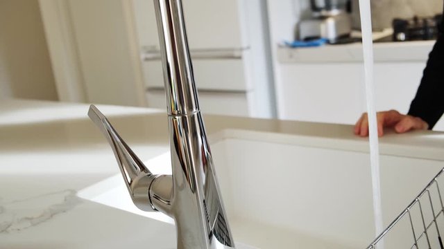 Closeup shot of caucasian woman hand opening and closing chrome faucet in a modern kitchen