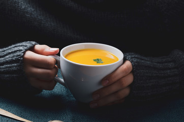 Female hand holding a  bowl with pumpkin cream soup. Cozy comfort concept.